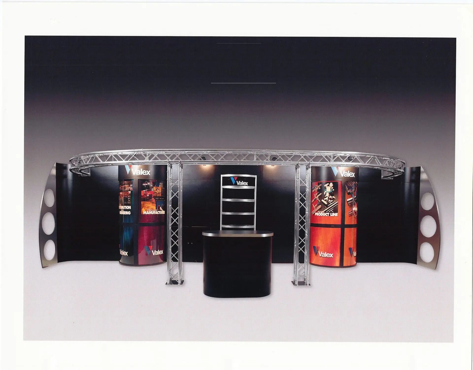 A trade show exhibit with a curved frame structure and large promotional graphics displayed on the walls. The center features a counter with shelving behind it, and "Valex" logos are visible on multiple panels. The setup is well-lit, creating a sleek and professional look.